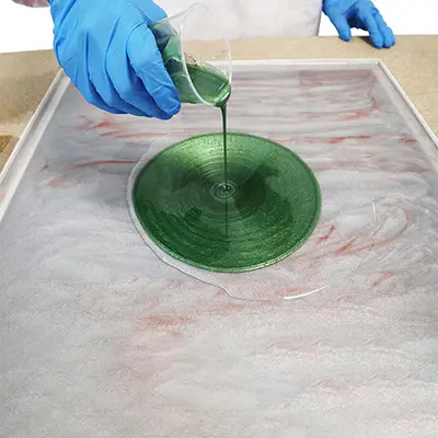 Ein Kunstwerk aus Epoxidharz wird mit grün eingefärbten Epoxidharz übergossen 
