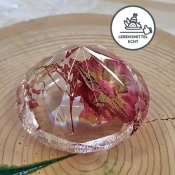 Glasklarer diamantgeformtes Objekt, welches eine Blume beinhaltet und auf einer Holzscheibe liegt